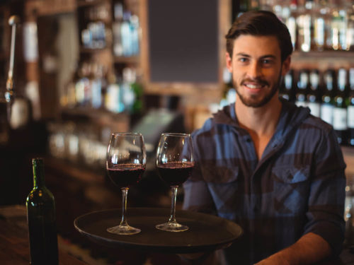 Junger Weinbarbesitzer mit zwei Gläsern Rotwein, der Yoveletta, die Cloudkasse für deine Bar benutzt.